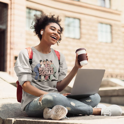 Woman sitting outdoors with a laptop and coffee, wearing a 'Nurse Squad' t-shirt.