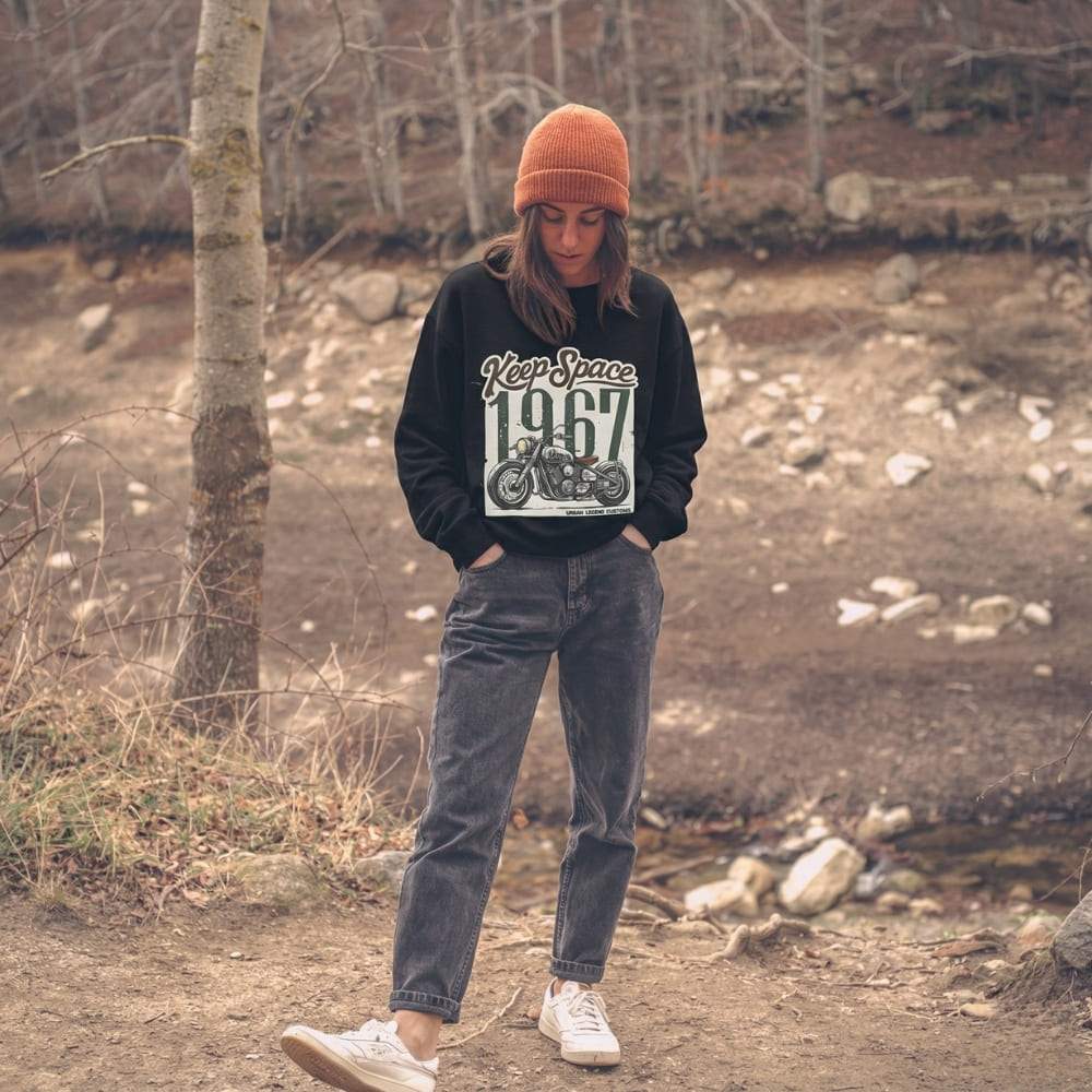 Person wearing a black sweatshirt with a graphic design, standing in a forested area.