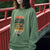 Person wearing a green sweatshirt with a graphic design in front of a red bridge.