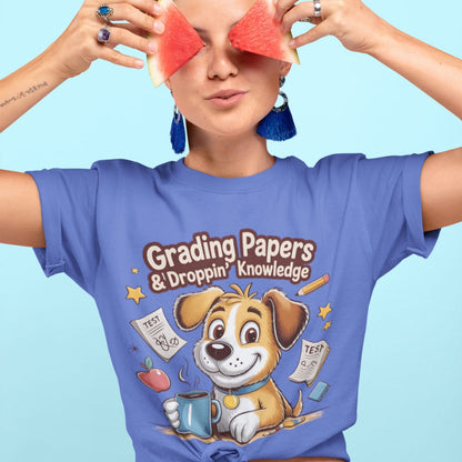 Person wearing a blue t-shirt with a cartoon dog design and text, holding watermelon slices over their eyes against a light blue background.