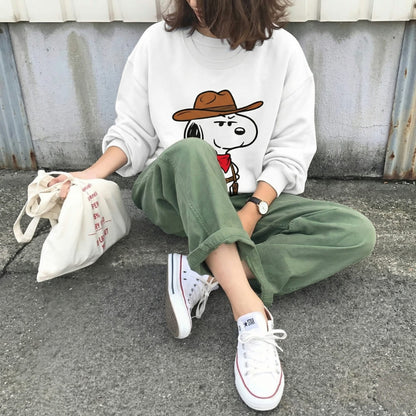 Person wearing a white sweatshirt with a cartoon character, green pants, and white sneakers sitting on the ground.