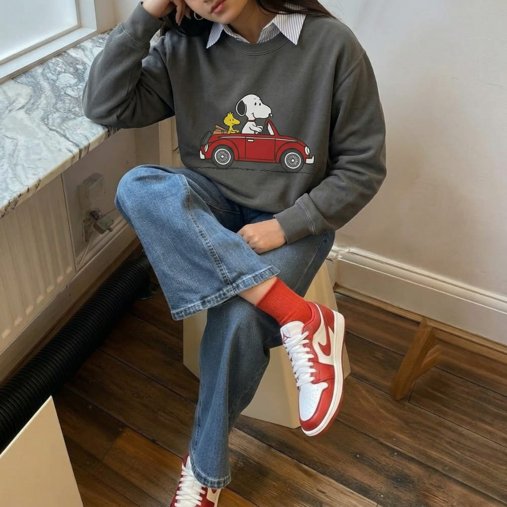 Person wearing a gray sweatshirt with a cartoon design, sitting on a step indoors.