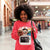 Woman in a pink sweatshirt with a graphic design, using a smartphone in an indoor setting.