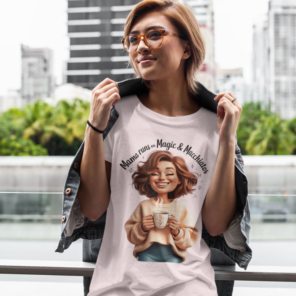 Woman wearing a t-shirt with a graphic design of a woman holding a coffee cup, with text 'Mama runs on magic & macchiatos' in an urban setting.