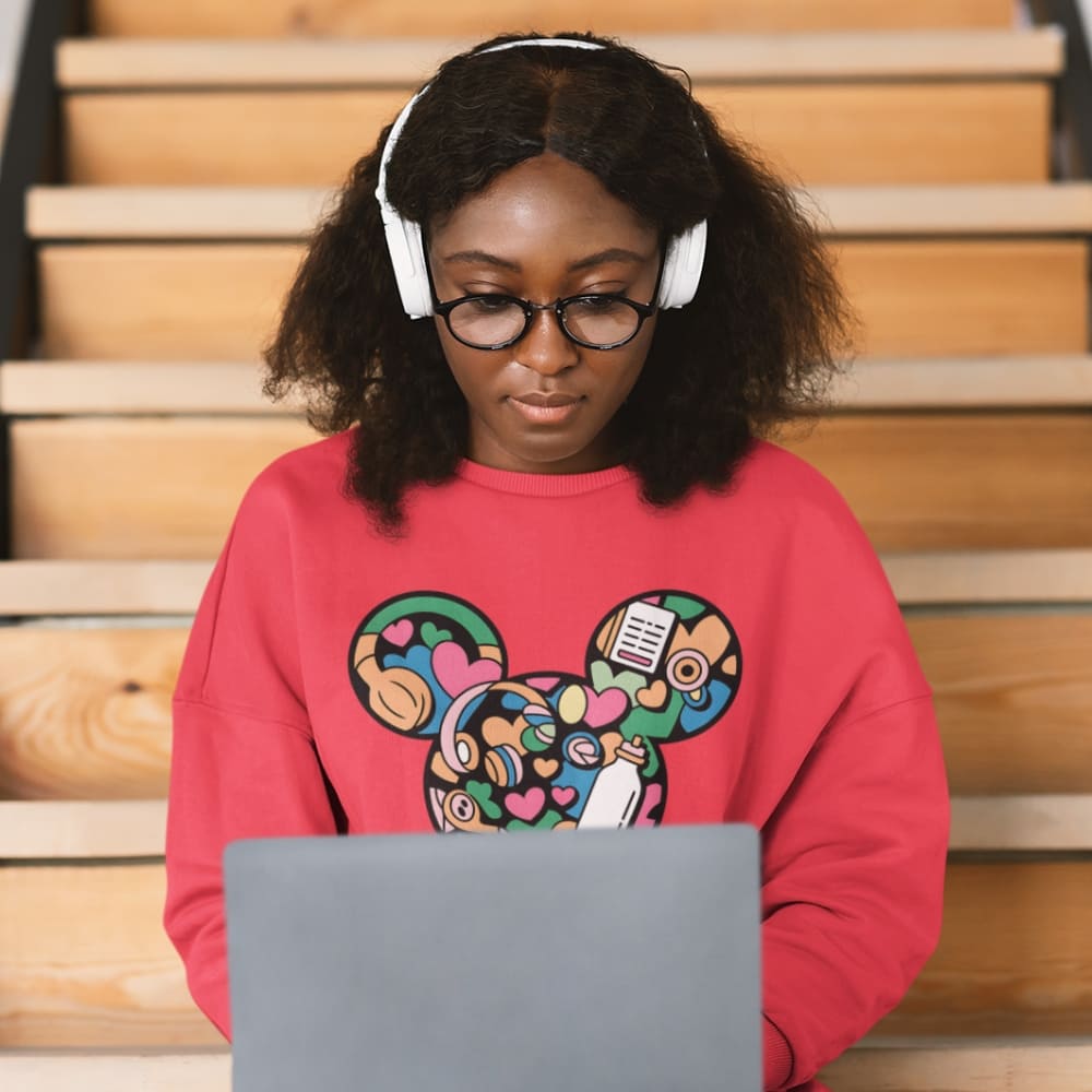 Person wearing a colorful sweatshirt with a design, sitting on steps using a laptop.