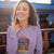 Woman wearing a purple sweatshirt with a coffee-themed design and text.