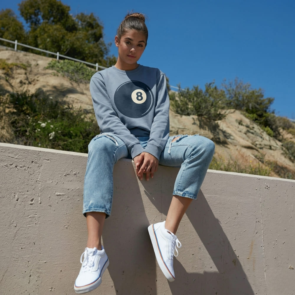 Person sitting on a ledge outdoors with a blue sweatshirt featuring the number 8.