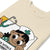 Beige t-shirt with a cartoon character and medical-themed design on a white background