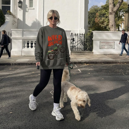 Woman walking a dog on a street wearing a sweatshirt with 'Wild Bunch' text.