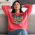 Woman wearing a red sweatshirt with text sitting on a couch.