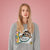 Person wearing a gray sweatshirt with a graphic design on a pink background