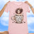 Pink t-shirt with a graphic of a person holding a coffee mug and text 'Don't ask me anything before a cup of 2', held up against a blue sky background.