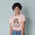 Person wearing a pink t-shirt with a graphic design and text, standing against a plain background