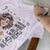 Lavender t-shirt with graphic design and text held by a person