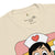 Beige t-shirt with cartoon character wearing a nurse's hat and red heart on a white background