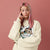 Person wearing a cream sweatshirt with a graphic design on a pink background