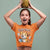 Person wearing an orange t-shirt with a cartoon dog holding a pineapple above their head on a gray background