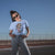 Woman wearing a light blue t-shirt with a graphic design outdoors against a clear blue sky.