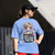 Person wearing a blue t-shirt with a graphic design and text, standing outdoors.