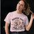 Woman wearing a pink t-shirt with a graphic design and text.