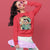 Person wearing a red sweatshirt with a cartoon character design, holding a pink skateboard against a red background