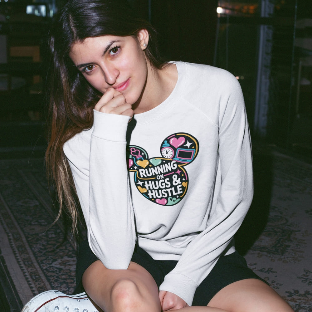 Woman wearing a white sweatshirt with colorful design and text sitting on the floor.
