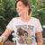 Woman wearing a t-shirt with a graphic design and text, sitting outdoors.