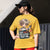 Person wearing a yellow t-shirt with a graphic design and text, standing outdoors.