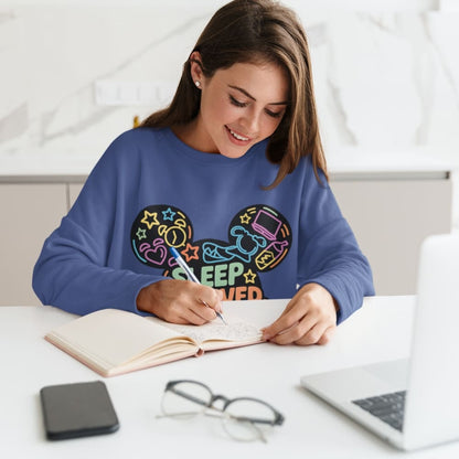 Woman in a blue sweatshirt with colorful graphics writing in a notebook at a desk.