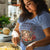 Woman wearing a blue t-shirt with a graphic design, standing in a kitchen.