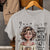 Gray t-shirt with a graphic of a woman holding a coffee cup and text, hanging on a wooden hanger.