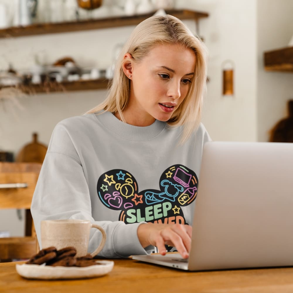Woman wearing a sweatshirt with a colorful design sitting at a table with a laptop and coffee.