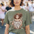 Person wearing a green t-shirt with a graphic design of a person in a coffee cup and text.