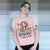 Person wearing a pink t-shirt with a graphic design and text.