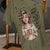 Khaki t-shirt with a graphic of a woman holding a mug and text, hanging on a wooden chair.