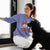 Woman wearing a purple sweatshirt with text sitting next to a black dog indoors.
