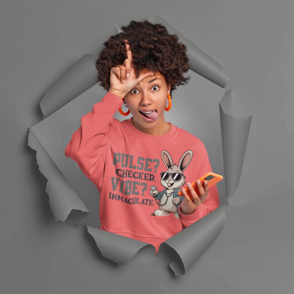 Person wearing a pink sweatshirt with a graphic design, standing through a torn paper effect on a gray background.