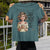 Person holding a teal t-shirt with a graphic of a woman holding a mug and text.