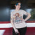 Person wearing a t-shirt with a graphic design and text, standing indoors.