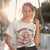 Woman wearing a t-shirt with a graphic design and text, standing outdoors.