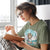 Woman reading a book while wearing a green t-shirt with a graphic design.