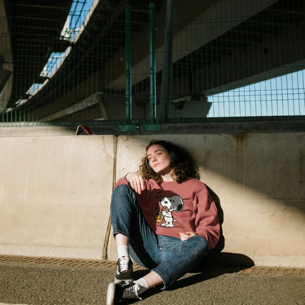 Person wearing a red sweatshirt with a graphic design, sitting against a concrete wall.