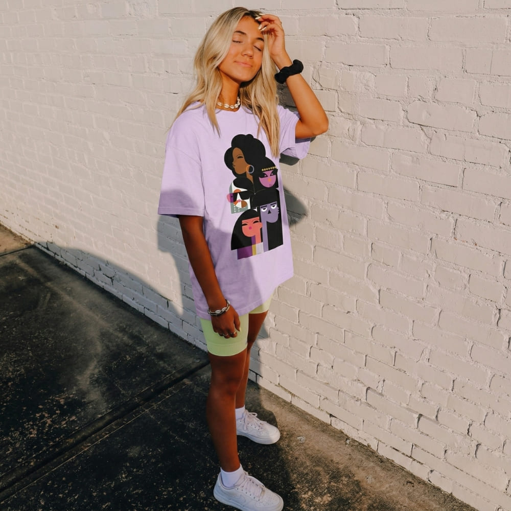 Woman wearing a purple t-shirt with graphic designs against a white brick wall.