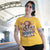 Person wearing a yellow t-shirt with a graphic design and text in an indoor setting