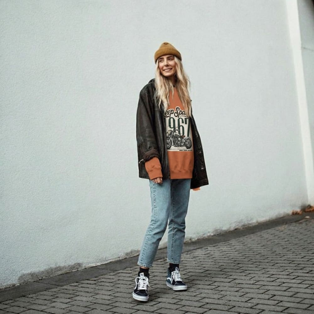 Person wearing a stylish outfit with a beanie, jacket, and jeans against a plain wall.