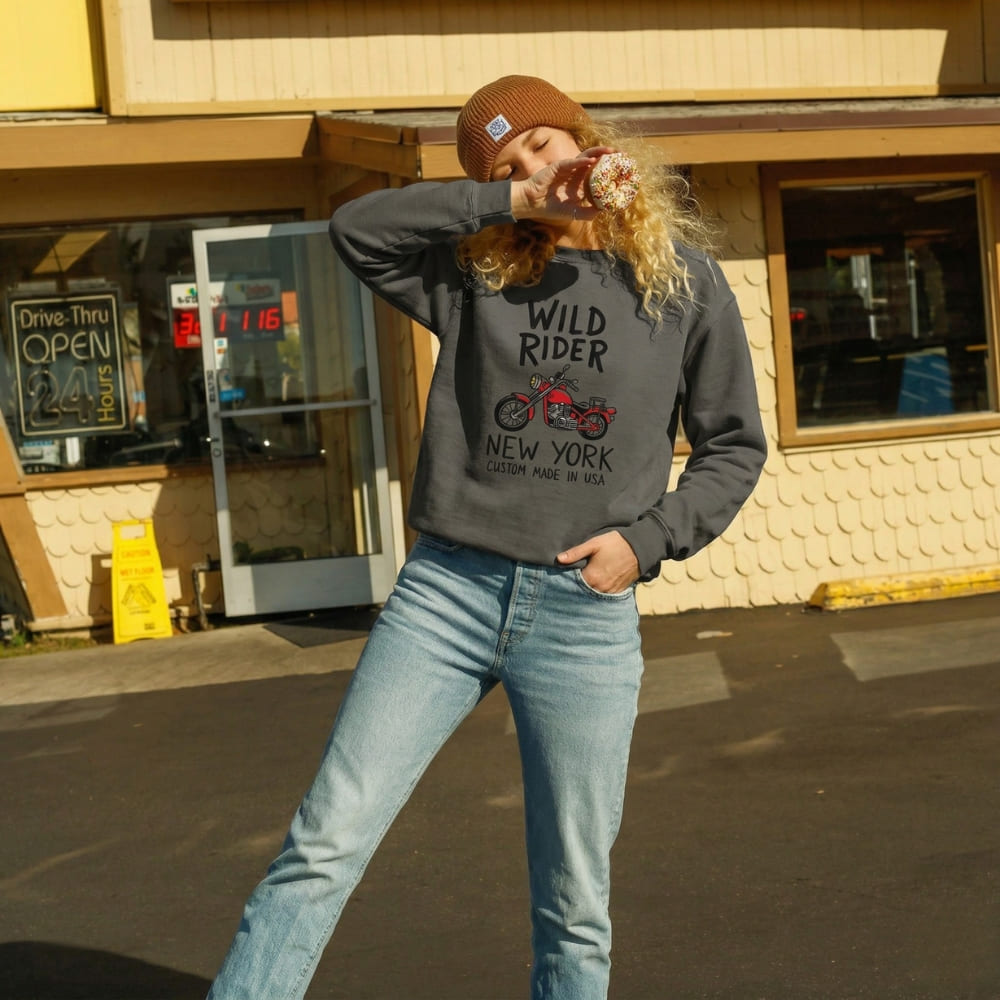 Person wearing a gray 'Wild Rider New York' sweatshirt in front of a drive-thru window.