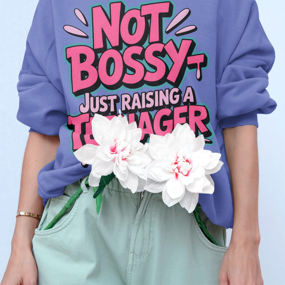 Person wearing a purple sweatshirt with 'Not Bossy Just Raising a Teenager' text, holding white flowers.
