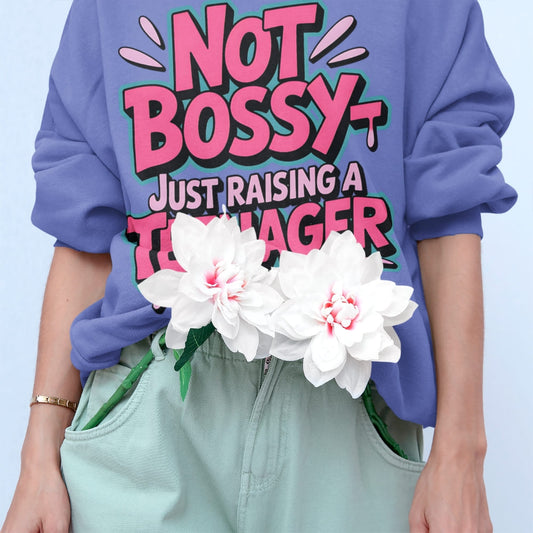 Person wearing a purple sweatshirt with 'Not Bossy Just Raising a Teenager' text, holding white flowers.