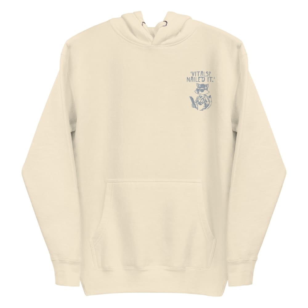 Raccoon nurse graphic wearing scrubs and sunglasses holding a clipboard under the quote “Vitals? Nailed It.” – printed on a black Cotton Heritage hoodie