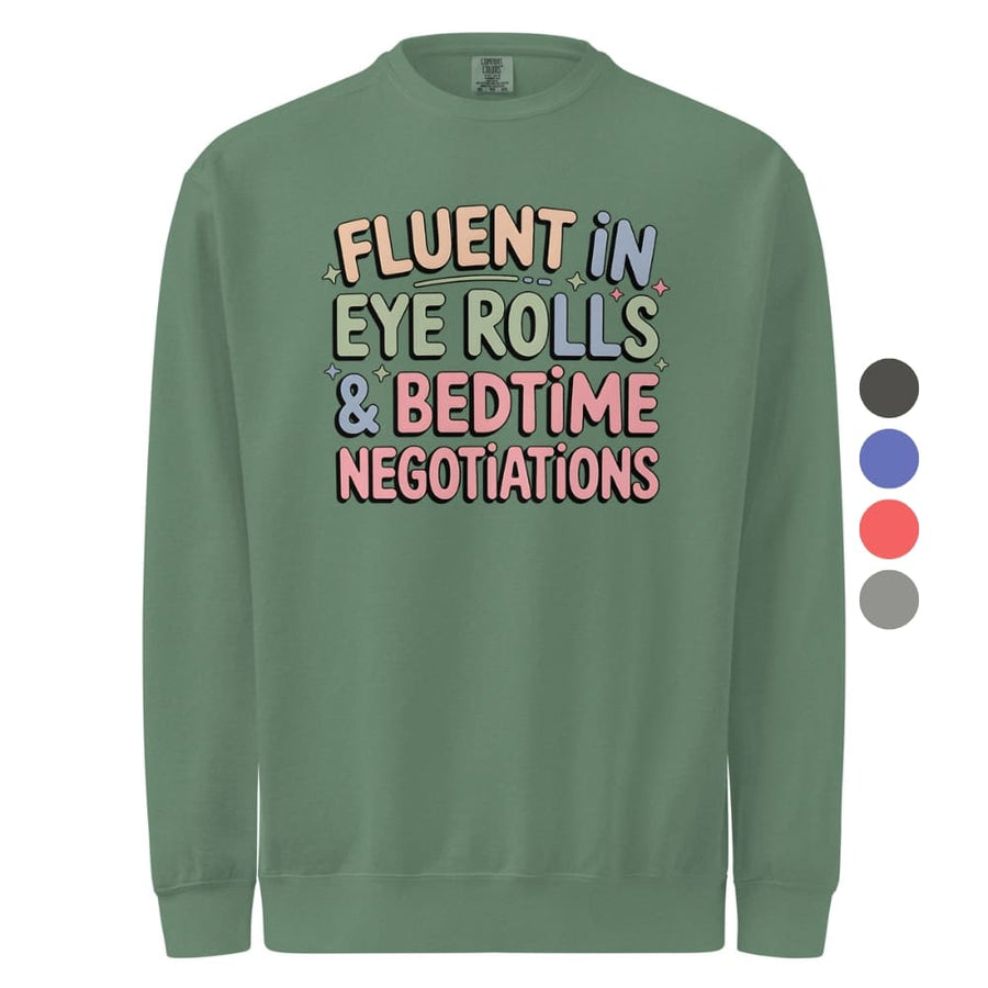 Green sweatshirt with colorful text 'FLUENT IN EYE ROLLS & BEDTIME NEGOTIATIONS' on a white background.